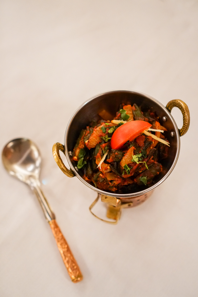 Bhindi masala in a brass karahi, with tomato wedge and ginger julienne.