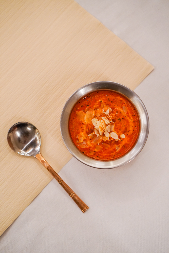 Butter chicken in a copper bowl, finished with slivered almonds and a swirl of cream.
